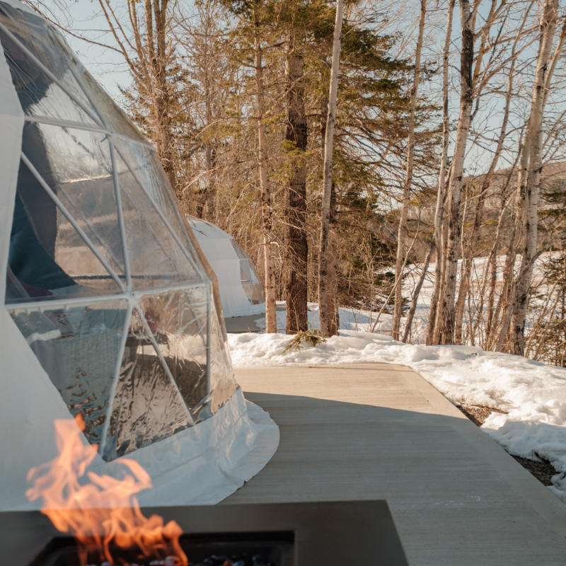 Stargazing Dome 23' Luna Glamping white by fireplace with snow in woods on wood deck
