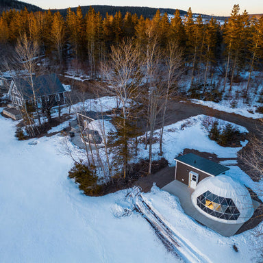 Stargazing Dome 23' Luna Glamping white drone view in forest with snow on concrete slab