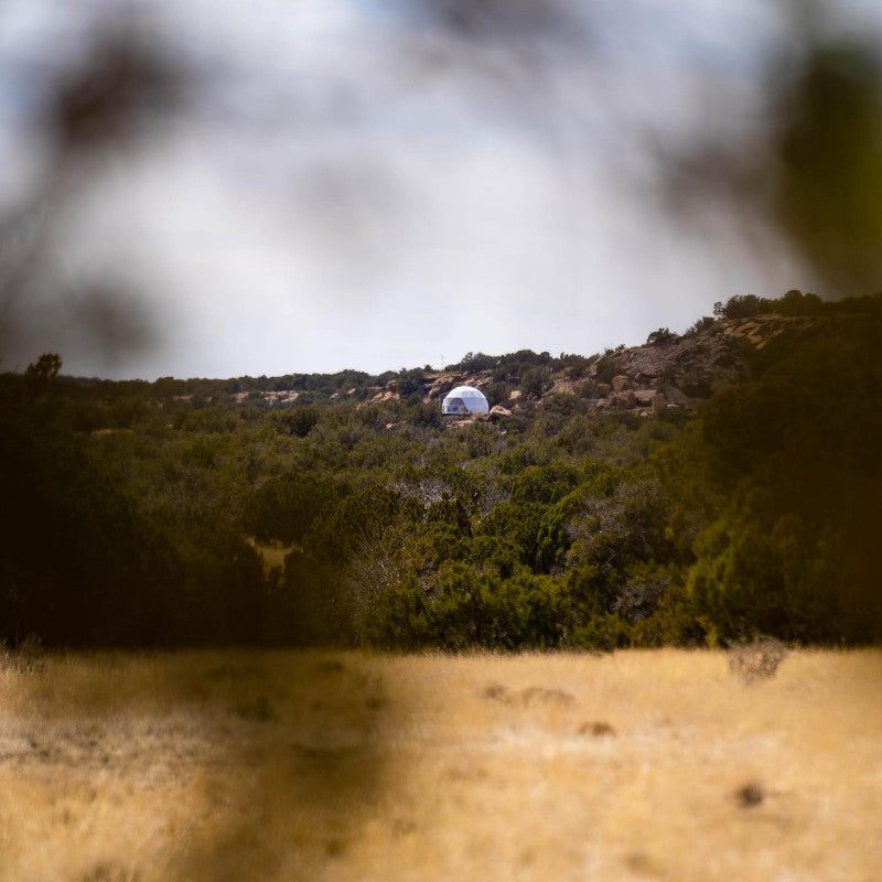 Stargazing Dome 23' Luna Glamping white front left long shot view in desert through trees